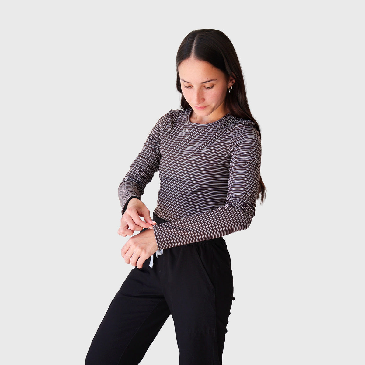 Fall Stripes CoreFit Underscrub, three-quarter view adjusting the cuff: long-sleeve top in fine taupe and black stripes